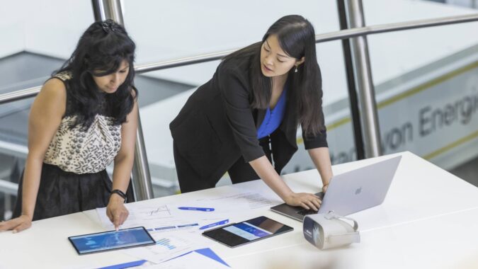 Zwei Frauen arbeiten gemeinsam an Laptop und Ipad stehend an einem Tisch