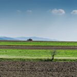 Ackerlandschaft mit Bergen im Hintergrund und einem Tracktor in der Ferne